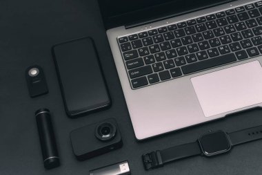 Bir grup multimedya aygıtı. Aksiyon kameralı bir laptop, akıllı bir telefon, akıllı bir saat ve siyah arka planda USB flash diski olan bir güç bankası.