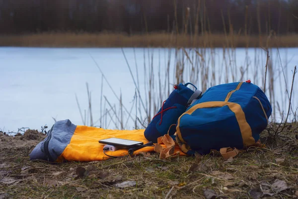 Smartphone is charged using a portable charger. Power Bank charges the phone outdoors with a backpack for tourism in the background of nature and the river