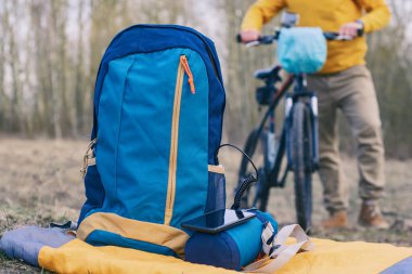 Taşınabilir şarj güç bankası, arka planda bisikletli bir bisikletçinin çantasıyla birlikte bir akıllı telefonu doğada şarj ediyor. Seyahat zamanı.