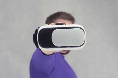 Adam sanal gerçeklik ve 360 derecelik video için elinde gözlük tutuyor. Işık arkaplanındaki akıllı telefon için VR başlığı