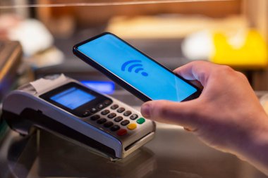 Müşteri, NFC teknolojisini kullanarak akıllı telefon ile ödeme yapıyor. Ödeme terminalinin arka planına karşı