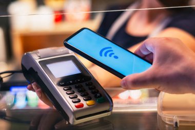 Müşteri, NFC teknolojisini kullanarak akıllı telefon ile ödeme yapıyor. Ödeme terminali ve satıcının kızı ile karşılaştırıldığında,