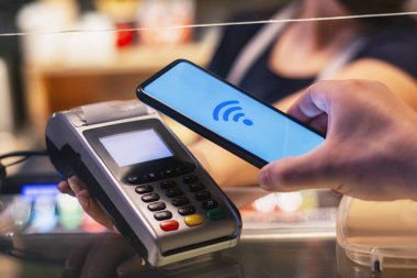 Müşteri, NFC teknolojisini kullanarak akıllı telefon ile ödeme yapıyor. Ödeme terminali ve satıcının kızı ile karşılaştırıldığında,