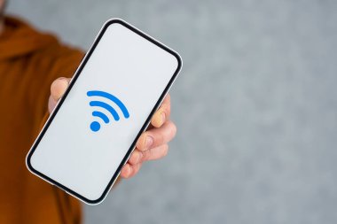 Gri arkaplanda kablosuz ağ ikonu olan bir telefon görüntüsü. Adam elinde akıllı bir telefon tutuyor.