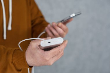Adamın elinde gri bir arka planda akıllı telefon ve taşınabilir şarj aleti var. Güç Bankası telefonu şarj ediyor