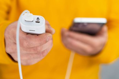 Adamın elinde gri bir arka planda akıllı telefon ve taşınabilir şarj aleti var. Güç Bankası telefonu şarj ediyor