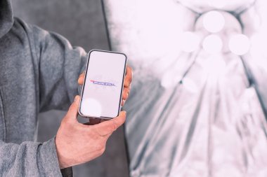 Stüdyo ışıklarının arka planına bir son dakika haber simgesi yerleştirilmiş telefon ekranı. Bir adam elinde bir akıllı telefonun maketini tutuyor.