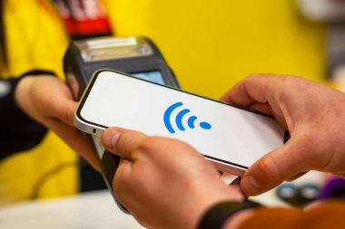 Müşteri, NFC teknolojisini kullanarak akıllı telefon ile ödeme yapıyor. Ödeme terminali ve satıcının kızı ile karşılaştırıldığında,