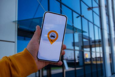 Otoparktaki yolcu mobil uygulamalı bir akıllı telefon tutuyor ve internetten taksi çağırıyor.