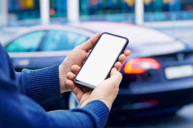 Adamın elinde bir akıllı telefon var. Arabanın arka planında beyaz ekran olan telefonu taklit et