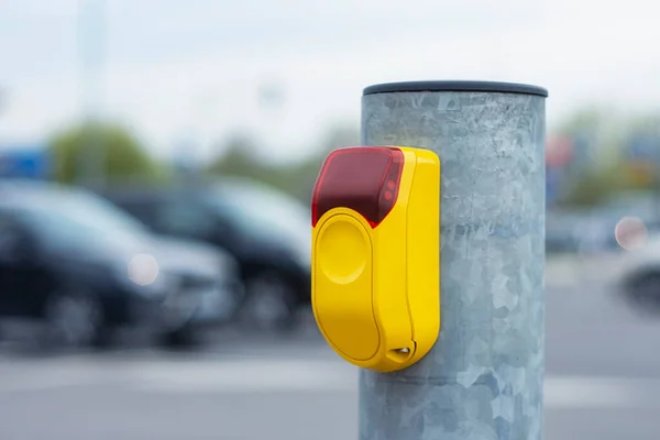 Yellow button at a traffic light for pedestrians on the background of a road with cars