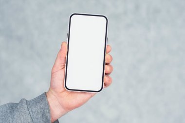 Gri kazaklı adam arka planda beyaz ekran yakın plan ile akıllı telefonun bir kopyasını tutuyor.
