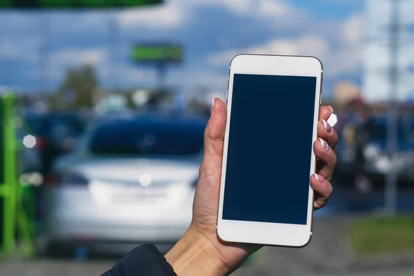 Kızın elinde bir akıllı telefon var. Şarj istasyonunda beyaz ekranlı telefonu elektrikli arabanın arka planına uydur