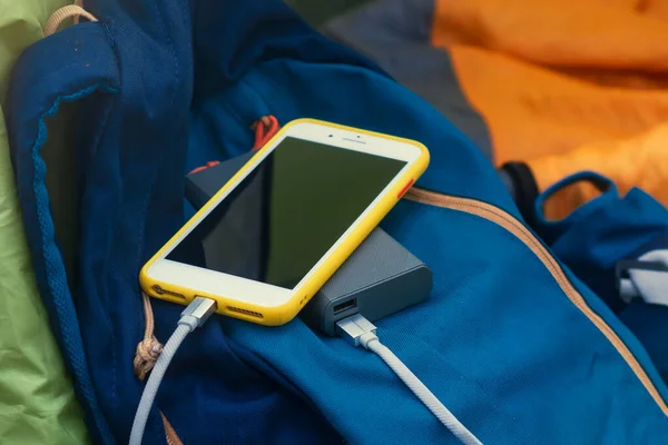 Akıllı telefon taşınabilir şarj aleti ile şarj edilir. Elektrik Bankası açık havada telefon faturasını turizm için bir sırt çantasıyla kesiyor.