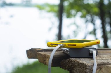 Taşınabilir şarj aleti. Enerji Bankası, doğanın arka planında, ahşap bir masada akıllı bir telefonu şarj ediyor. Turizm konsepti