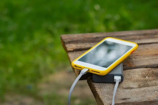 ポータブル旅行充電器 電力銀行は 自然を背景に 木製のテーブルの上でスマートフォンを充電します 観光をテーマにしたコンセプト — ストック写真