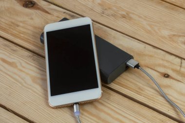 Taşınabilir şarj aleti ahşap bir masada akıllı telefonu şarj ediyor. Koyu ekran ve güç bankasıyla cep telefonu modeli