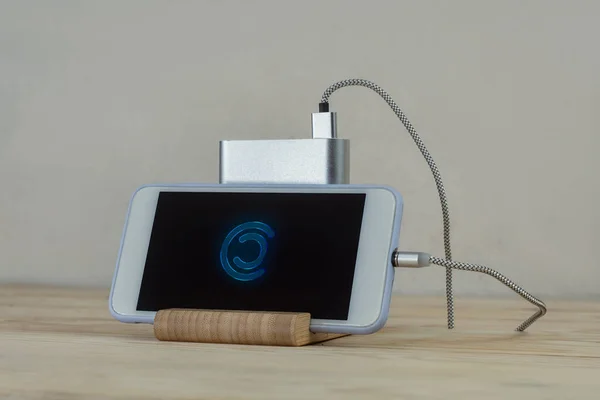 ポータブル充電器は木製のテーブルの上にスマートフォンを充電します ダークスクリーンとパワーバンクと携帯電話のモックアップ — ストック写真