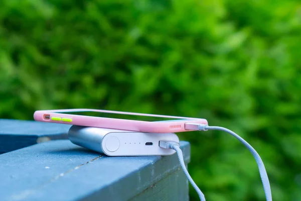 Portable charger charges a smartphone on a wooden railing. Mobile phone mockup with dark screen and power bank