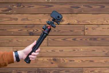 Ahşap bir arka planda, elinde esnek bir tripodun üzerindeki sıkıştırılmış aksiyon kamerası.