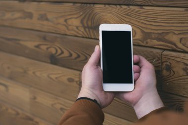 Adam elinde ahşap bir arka planda siyah ekranlı akıllı bir telefonun maketini tutuyor.