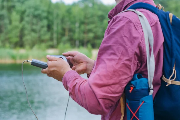 남자는 스마트폰을 휴대용 충전기를 있습니다 호수가 자연의 배경에 — 스톡 사진