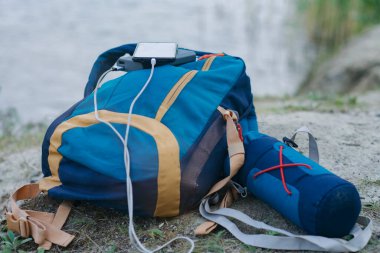 Akıllı telefon taşınabilir şarj aleti ile şarj edilir. Elektrik Bankası açık havada telefon faturasını doğa ve nehir arka planında turizm için bir sırt çantasıyla ödüyor.