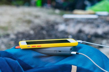 Akıllı telefon taşınabilir şarj aleti ile şarj edilir. Elektrik Bankası açık havada telefon faturasını turizm için bir sırt çantasıyla kesiyor.