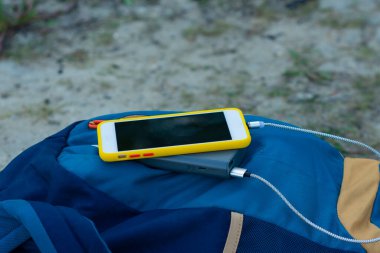 Akıllı telefon taşınabilir şarj aleti ile şarj edilir. Elektrik Bankası açık havada telefon faturasını turizm için bir sırt çantasıyla kesiyor.