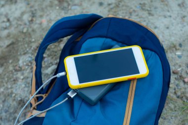 Akıllı telefon taşınabilir şarj aleti ile şarj edilir. Elektrik Bankası açık havada telefon faturasını turizm için bir sırt çantasıyla kesiyor.