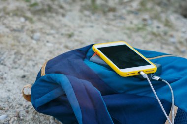Akıllı telefon taşınabilir şarj aleti ile şarj edilir. Elektrik Bankası açık havada telefon faturasını turizm için bir sırt çantasıyla kesiyor.