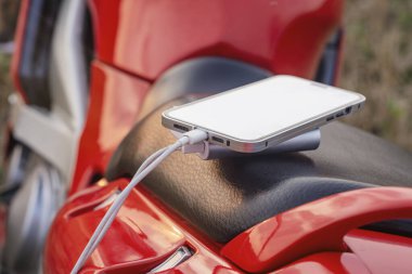 Motorsikletli akıllı telefon ve elektrik bankası telefonu doğanın arka planına karşı şarj ediyor.