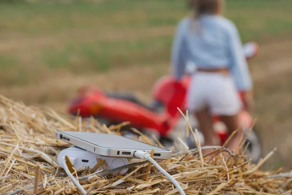 Smartphone close-up with a portable charger. Power Bank charges the phone against the backdrop of a motorcycle, a girl and nature