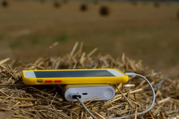 パワーバンクは屋外の干し草のフィールドでスマートフォンを充電します — ストック写真