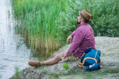 Turist bir sırt çantasıyla gölün kıyısında oturur. Turizm konsepti