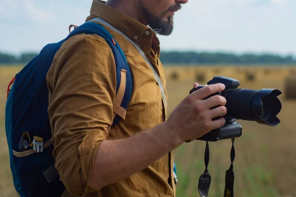 Traveler photographer with a camera in his hand against the background of a field and haystacks