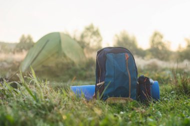 Doğa ve ormanın arka planında turist çadırı olan bir halı içeren spor sırt çantası.