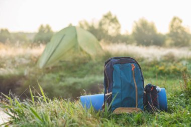 Doğa ve ormanın arka planında turist çadırı olan bir halı içeren spor sırt çantası.