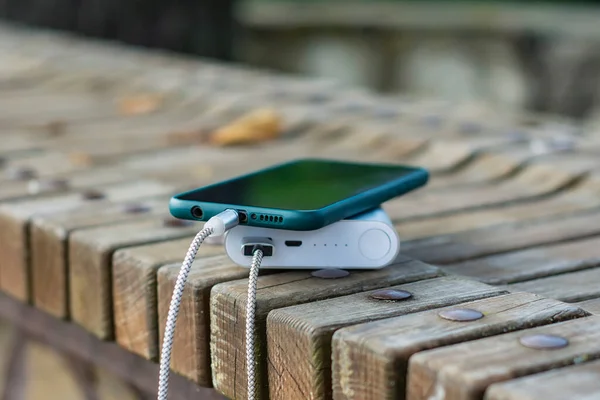 公園内の木製のベンチでスマートフォンを充電します — ストック写真