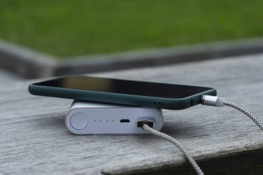 Güç Bankası parktaki ahşap bir bankta akıllı telefondan para alıyor.