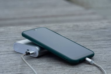 Güç Bankası parktaki ahşap bir bankta akıllı telefondan para alıyor.