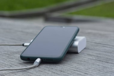 Güç Bankası parktaki ahşap bir bankta akıllı telefondan para alıyor.