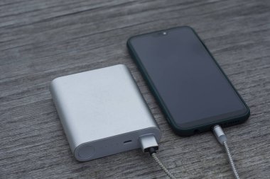 Güç Bankası parktaki ahşap bir bankta akıllı telefondan para alıyor.