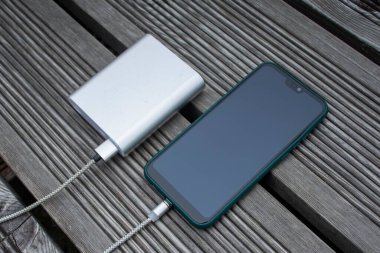 Güç Bankası parktaki ahşap bir bankta akıllı telefondan para alıyor.