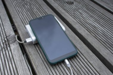 Güç Bankası parktaki ahşap bir bankta akıllı telefondan para alıyor.