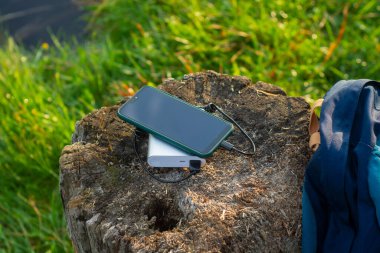 Akıllı telefon taşınabilir şarj aleti ile şarj edilir. Elektrik Bankası açık havada telefon faturasını turizm için bir sırt çantasıyla kesiyor.