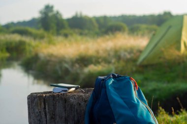 Akıllı telefon taşınabilir şarj aleti ile şarj edilir. Güç Bankası açık havada bir çadırın arka planına karşı bir sırt çantasıyla telefonu şarj ediyor.