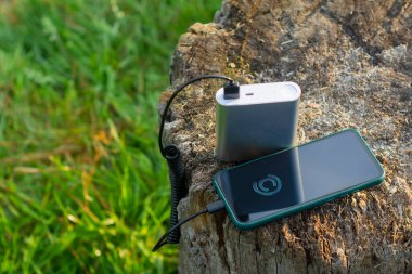 Akıllı telefon taşınabilir şarj aleti ile şarj edilir. Elektrik Bankası açık havada telefon faturasını turizm için bir sırt çantasıyla kesiyor.