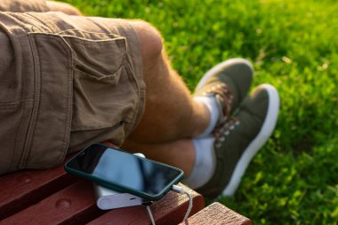 Adam elinde bir güç bankasıyla akıllı telefonu şarj ediyor. Cihazları şarj etmek için taşınabilir şarj cihazı