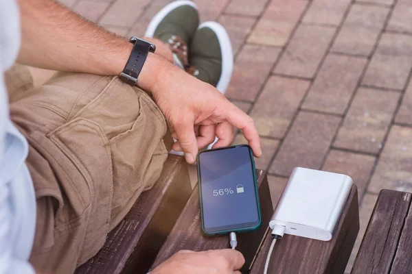 Adam elinde bir güç bankasıyla akıllı telefonu şarj ediyor. Cihazları şarj etmek için taşınabilir şarj cihazı
